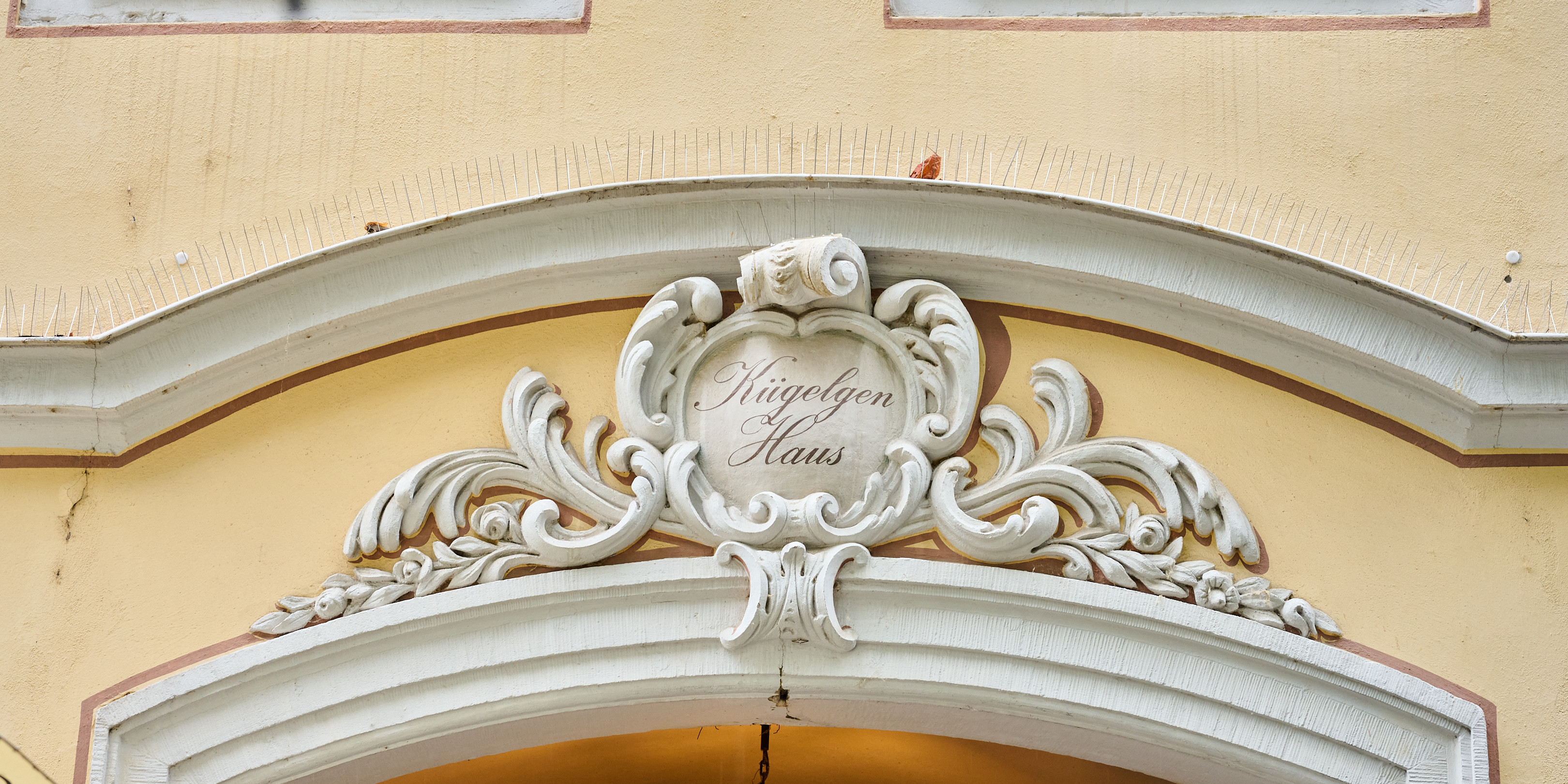 KI generiert: Das Bild zeigt eine kunstvolle Fassadenverzierung eines Gebäudes mit der Inschrift "Kriegelgen Haus". Der Hauptinhalt des Bildes ist die dekorative Architektur über einem Eingang.